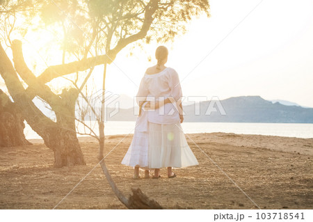Nice sisters, kid and teenage girl hugging and standing with their back together in the park  103718541