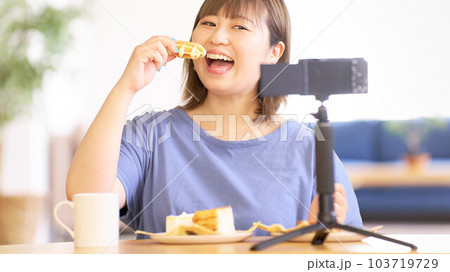 カメラで自分を撮影しながらスイーツを食べる若い女性 103719729