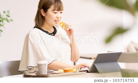 ワッフルを食べながらPC作業をする若い女性 103719735