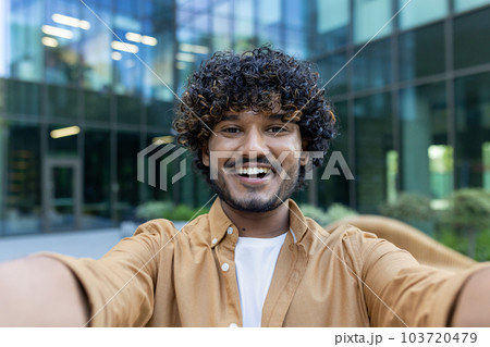 Online streaming. Close-up photo of a young Latin American man filming a blog, recording a podcast on the street. Smiling and talking to the camera. Online streaming. Close-up photo of a young Latin American man filming a blog, recording a podcast on the street. Smiling and talking to the camera. 103720479