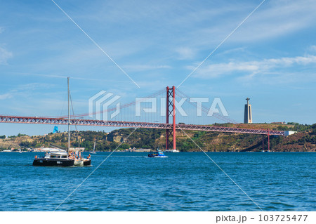 View of 25 de Abril Bridge famous tourist landmark over Tagus river, Christ the King monument and a tourist yacht boat. Lisbon, Portugal View of 25 de Abril Bridge famous tourist landmark over Tagus river, Christ the King monument and a tourist yacht boat. Lisbon, Portugal 103725477