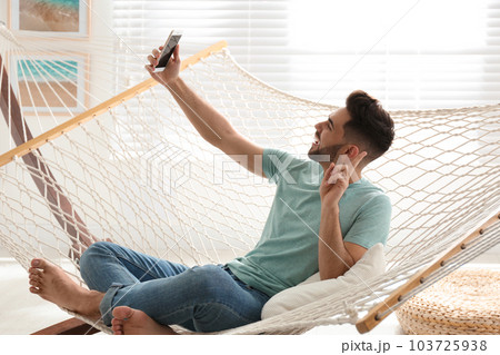 Young man taking selfie in hammock at home 103725938