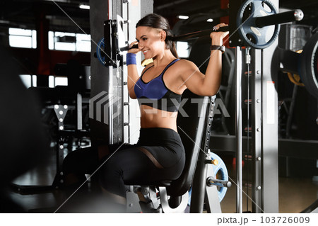 Young woman working out on Smith machine in modern gym 103726009