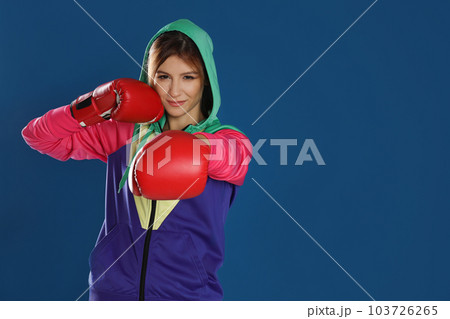 Young woman with boxing gloves on blue background, space for text 103726265