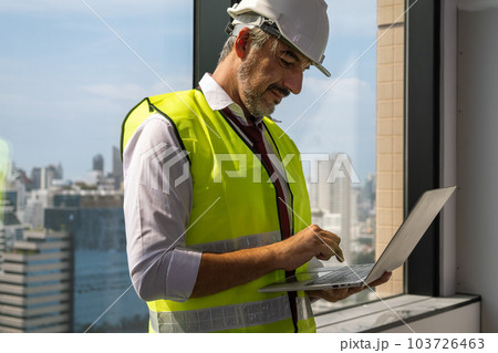 Close up view of male engineer with safety vest holding computer laptop working Close up view of male engineer with safety vest holding computer laptop working 103726463