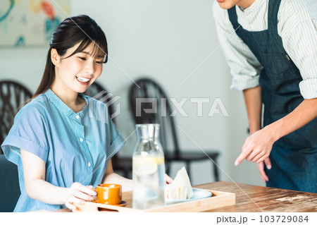 カフェでブランチを取る若い女性とエプロン姿の店員 カフェでブランチを取る若い女性とエプロン姿の店員 103729084