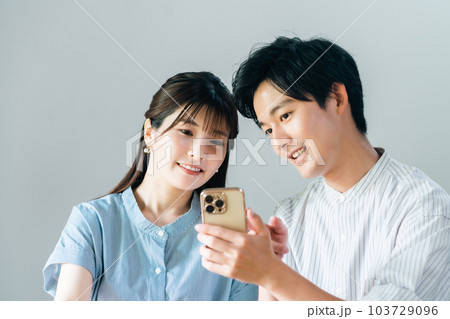 スマホの画面を見ながら話すカップル 103729096