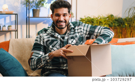 Happy indian man shopper unpacking cardboard box delivery parcel online shopping purchase at home 103729297