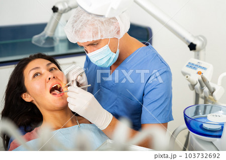 Man dentist examines a female patient with the help of working tools Man dentist examines a female patient with the help of working tools 103732692