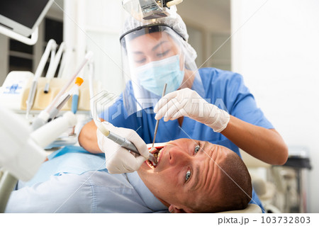 Female dentist drilling tooth to male patient Female dentist drilling tooth to male patient 103732803