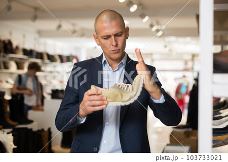 Interested man checking softness of sole of moccasins in shoe store 103733021