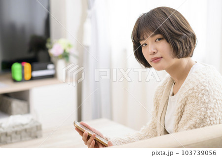 リビングでスマホを見る若い女性 103739056