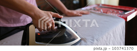 Female housewife ironing crumpled bedsheet on board using steam iron 103741370
