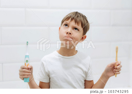 cute 8 years old boy holding bamboo and electric tooth brush making choice cute 8 years old boy holding bamboo and electric tooth brush making choice 103743295