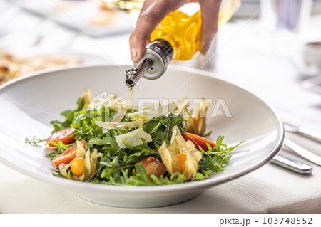 Olive oil pouring over a fresh rocket salad with parmesan shavings and physalis 103748552