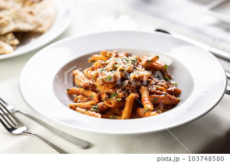 Pene alla arrabiata, Italian red sauce pasta served on a table in a plate with fresh grating of parmesan Pene alla arrabiata, Italian red sauce pasta served on a table in a plate with fresh grating of parmesan 103748580