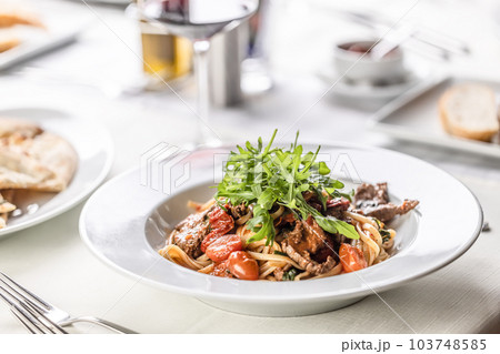 Italian coooking of linguine with meat, tomatoes and ruccola on top 103748585