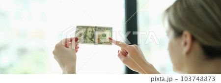Woman studying watermarks on money dollars in front of window closeup Woman studying watermarks on money dollars in front of window closeup 103748873