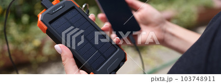 Hands holding solar power bank and mobile phone for recharging closeup Hands holding solar power bank and mobile phone for recharging closeup 103748911
