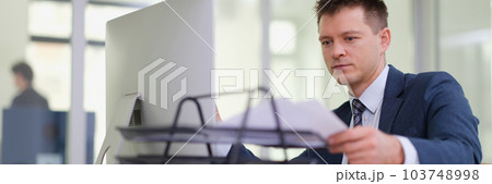 Businessman taking out paper from tray on desk in office 103748998