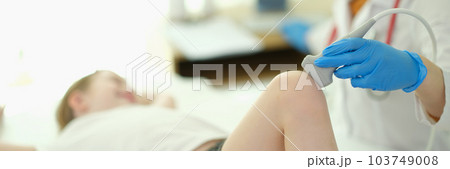 Doctor traumatologist making ultrasound examination of knee joint to child in clinic closeup 103749008