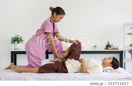 Body care treatment by thai massage. Cute girl with traditional dress stretch knee and leg by massager. Young asian woman relax in spa. Body care treatment by thai massage. Cute girl with traditional dress stretch knee and leg by massager. Young asian woman relax in spa. 103751627