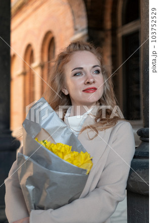 Portrait of smiling young woman with bouquet of yellow flowers outdoors. Date with beautiful girl. Vertical frame. Portrait of smiling young woman with bouquet of yellow flowers outdoors. Date with beautiful girl. Vertical frame. 103752529