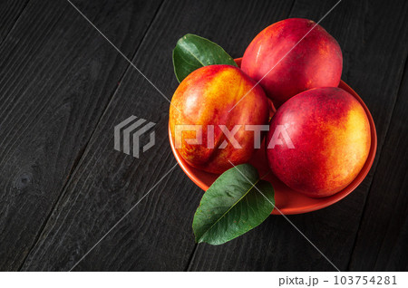 Three red ripe nectarine hybrids in their ripening season lie on orange plate or on a dark vintage table. 103754281