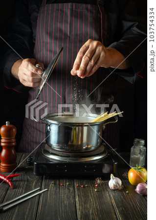 In the kitchen, dietary soup is prepared by the cook hands in a hot pot. The chef adds salt to the food 103754334