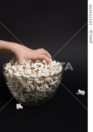 A child's hand reaches for popcorn in a glass bowl. 103754450