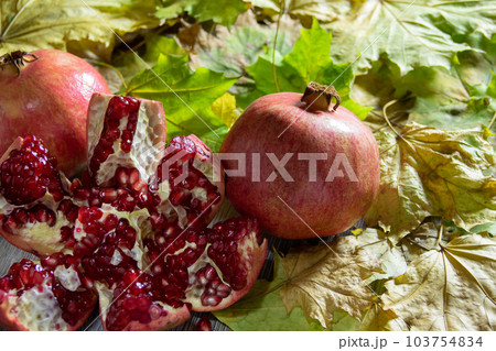 Two fresh ripe pomegranates and one cut on yellow autumn leaves 103754834