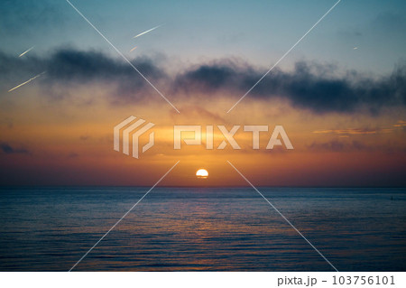 The sun rises over the a calm sea with dark clouds in the foreground The sun rises over the a calm sea with dark clouds in the foreground 103756101