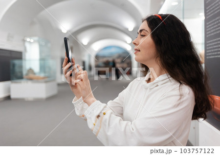 Side view of young Caucasian woman using smartphone. Concept of cultural exhibition and modern educational excursion 103757122