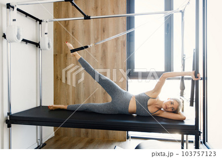Pregnant woman doing exercises with a special equipment. Fit blonde woman working out in a gym. Woman wearing grey sportive leggins and top. 103757123