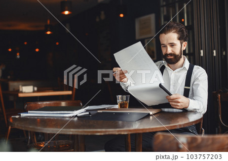 Man drinks whiskey. Businessman reads documents. Director in a shirt and suspenders. Man drinks whiskey. Businessman reads documents. Director in a shirt and suspenders. 103757203