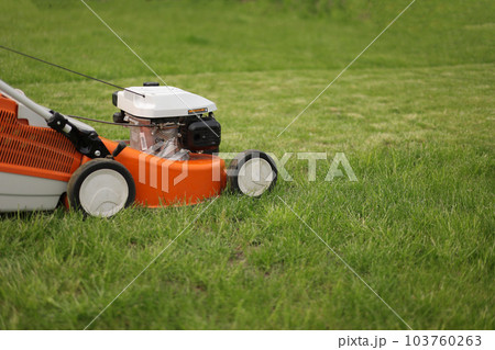 Close up orange-grey electric lawn mower on bright lush green lawn. Gardening work tools. Rotary lawn mower machine cut grass. Professional lawn care service. Place for text Close up orange-grey electric lawn mower on bright lush green lawn. Gardening work tools. Rotary lawn mower machine cut grass. Professional lawn care service. Place for text 103760263