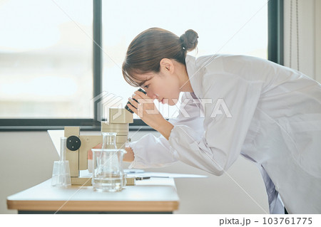 顕微鏡を覗く白衣の若い女性 103761775