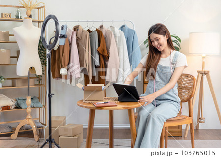 Female online seller is checking online clothes orders on tablet after using smartphone to broadcast live Female online seller is checking online clothes orders on tablet after using smartphone to broadcast live 103765015