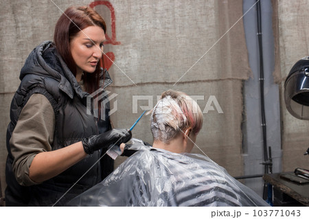 Pretty girl, professional hairdresser of European appearance, works with the client's hair, the process of dyeing hair in a barbershop Pretty girl, professional hairdresser of European appearance, works with the client's hair, the process of dyeing hair in a barbershop 103771043