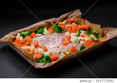 Raw sea bass fish fillet with salt, spices and vegetables in a baking dish 103771692