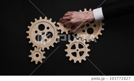 Closeup of a hand holding wooden gears against a black background Closeup of a hand holding wooden gears against a black background 103772827