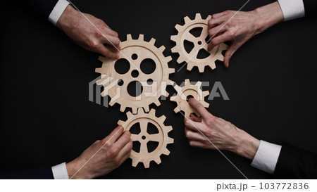 Group of business people connecting wooden cogwheels together on black background Group of business people connecting wooden cogwheels together on black background 103772836