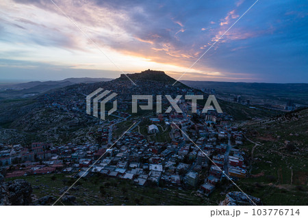トルコ　夕暮れ時のマルディンの旧市街の街並みと山頂に立つマルディン城と夕焼け空 103776714