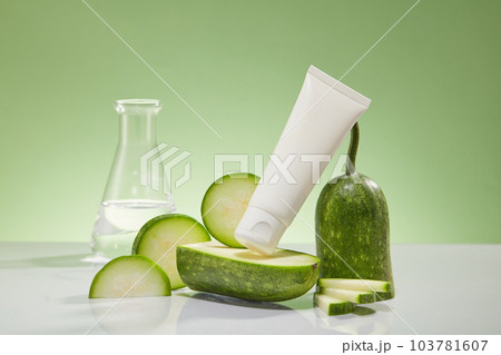 A white cosmetic tube with fresh winter melon slices and erlenmeyer flask displayed on a light green background. Winter melon helps to tighten skin, smooth skin, whiten pink and prevent acne. 103781607