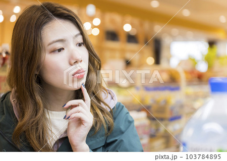 スーパーでどれを買おうか迷いながら買い物をする若い女性 103784895