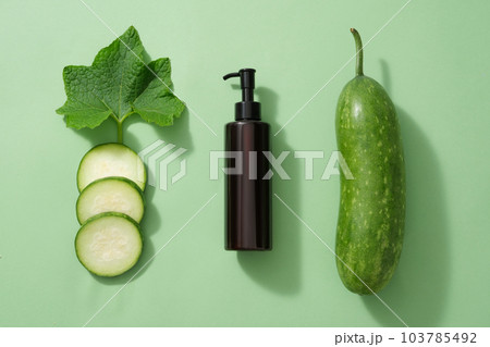 Minimal flat lay scene for advertising - an amber pump bottle with fresh winter melon, slices and leaf decorated on a light green background.  Advertising scene for cosmetic skin care and body care 103785492