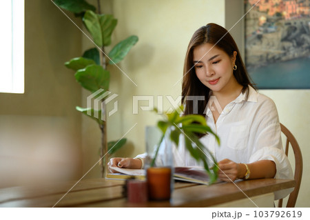 Serene young woman in casual clothes sitting in comfortable home interior and while reading novel of popular authors 103792619