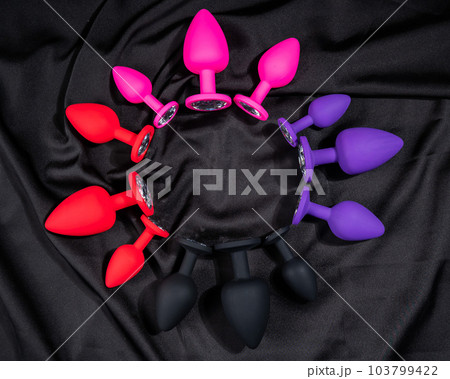 A set of silicone anal plugs in different colors and sizes on a black silk sheet.  103799422