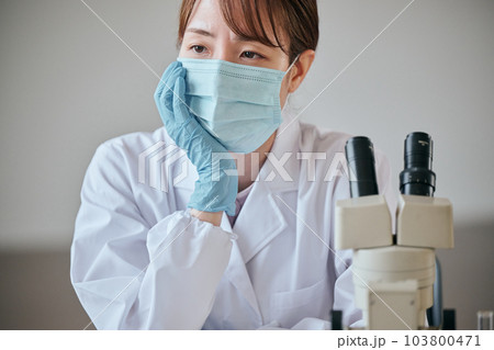 デスクで憂鬱そうな表情をする白衣の若い女性 103800471