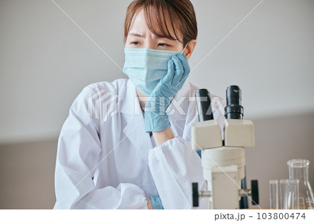 デスクで憂鬱そうな表情をする白衣の若い女性 103800474